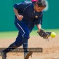 A female softball player wearing a dark blue uniform catches a yellow softball